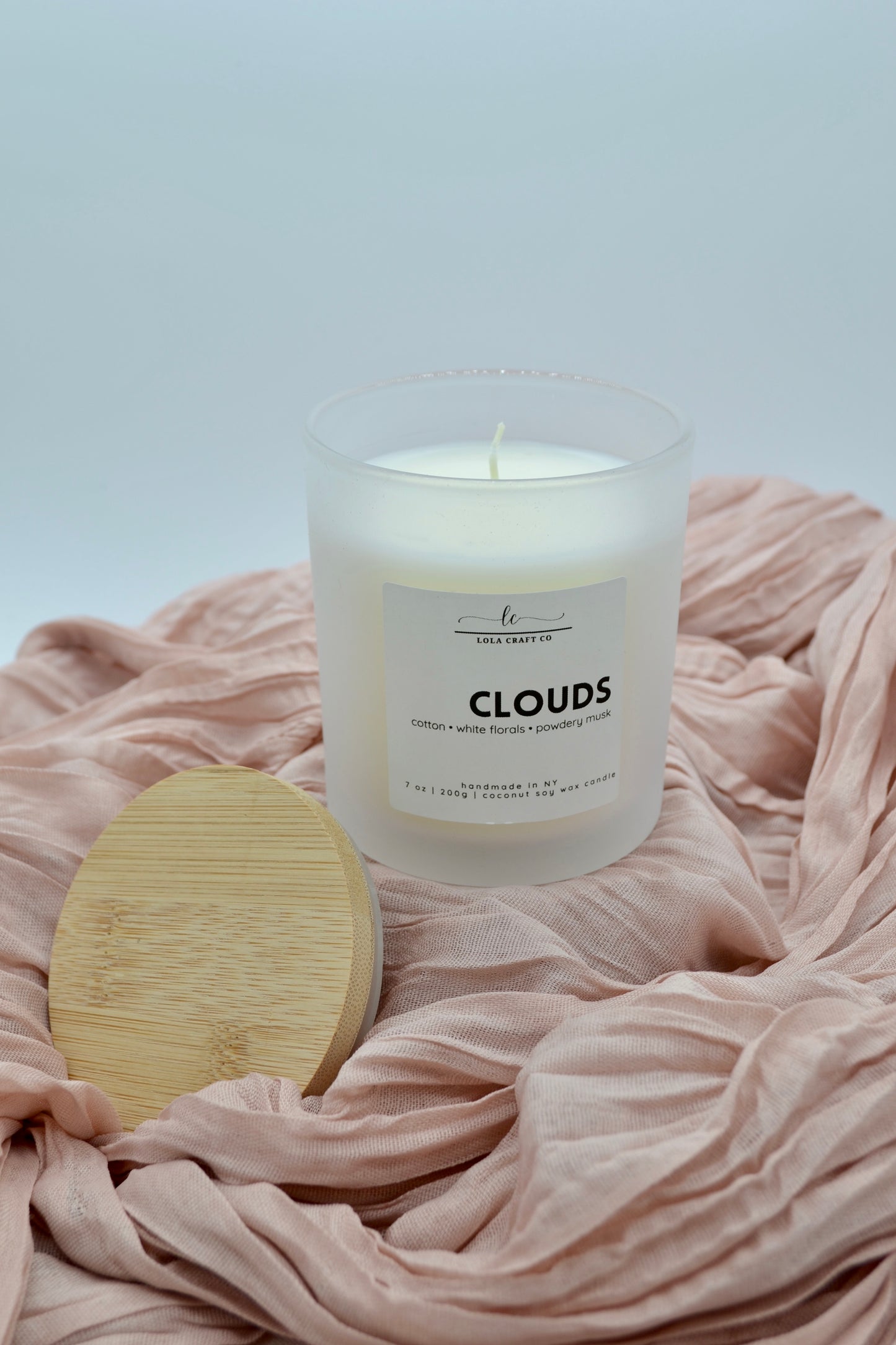 Candle labeled 'Clouds' on a soft pink fabric background