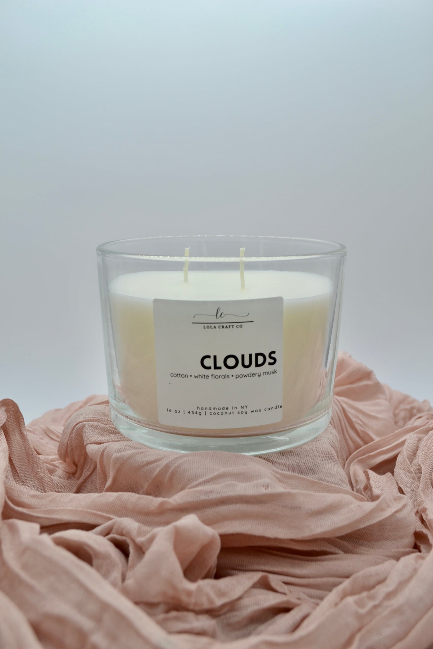 Candle labeled 'Clouds' on a soft pink fabric with a light gray background