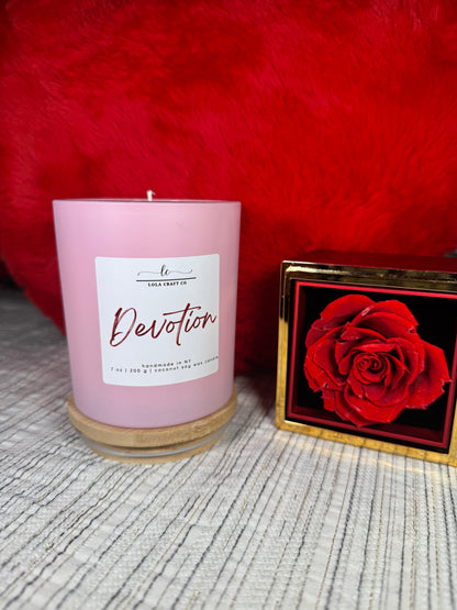 Pink candle labeled 'Devotion' with a red rose in the background on a textured surface.
