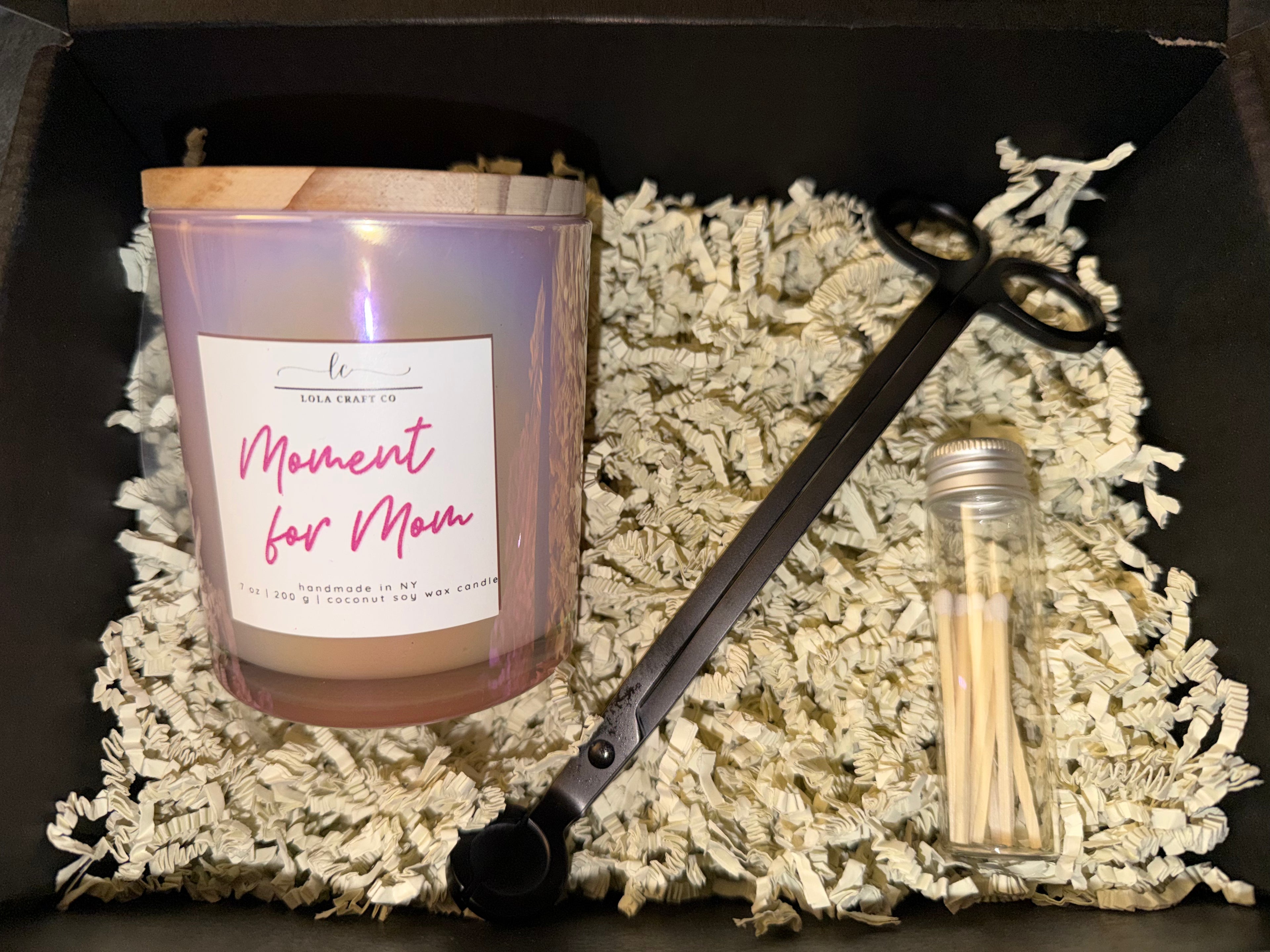 Candle with 'Moment for Mom' label, wick trimmers, and matches on a textured surface