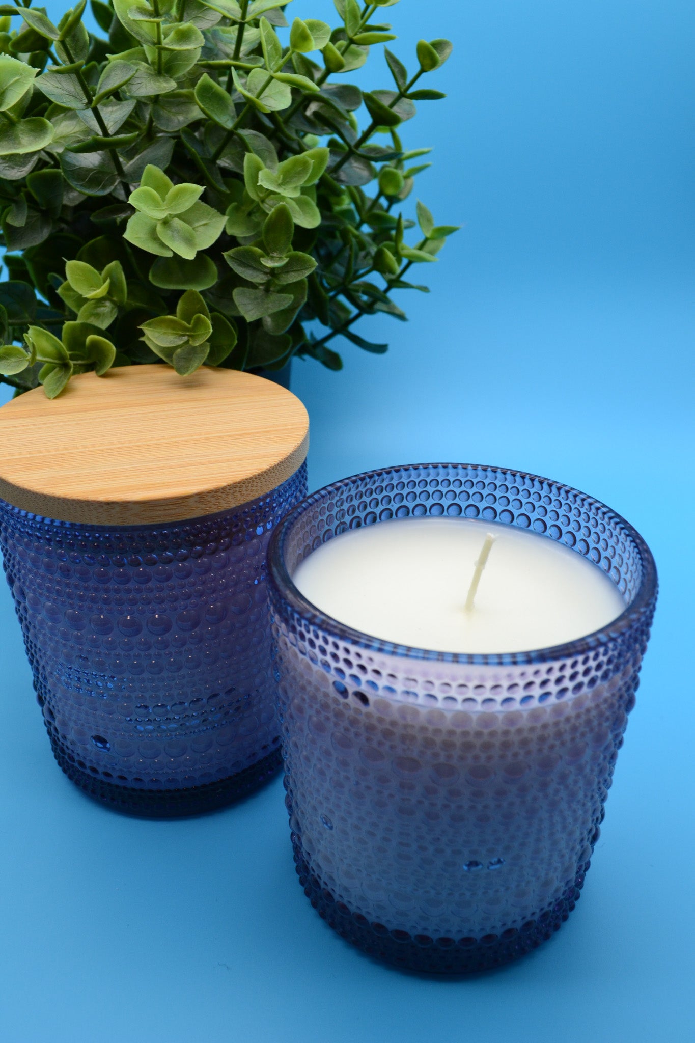 Two blue textured candle holders with a lit candle on a blue background