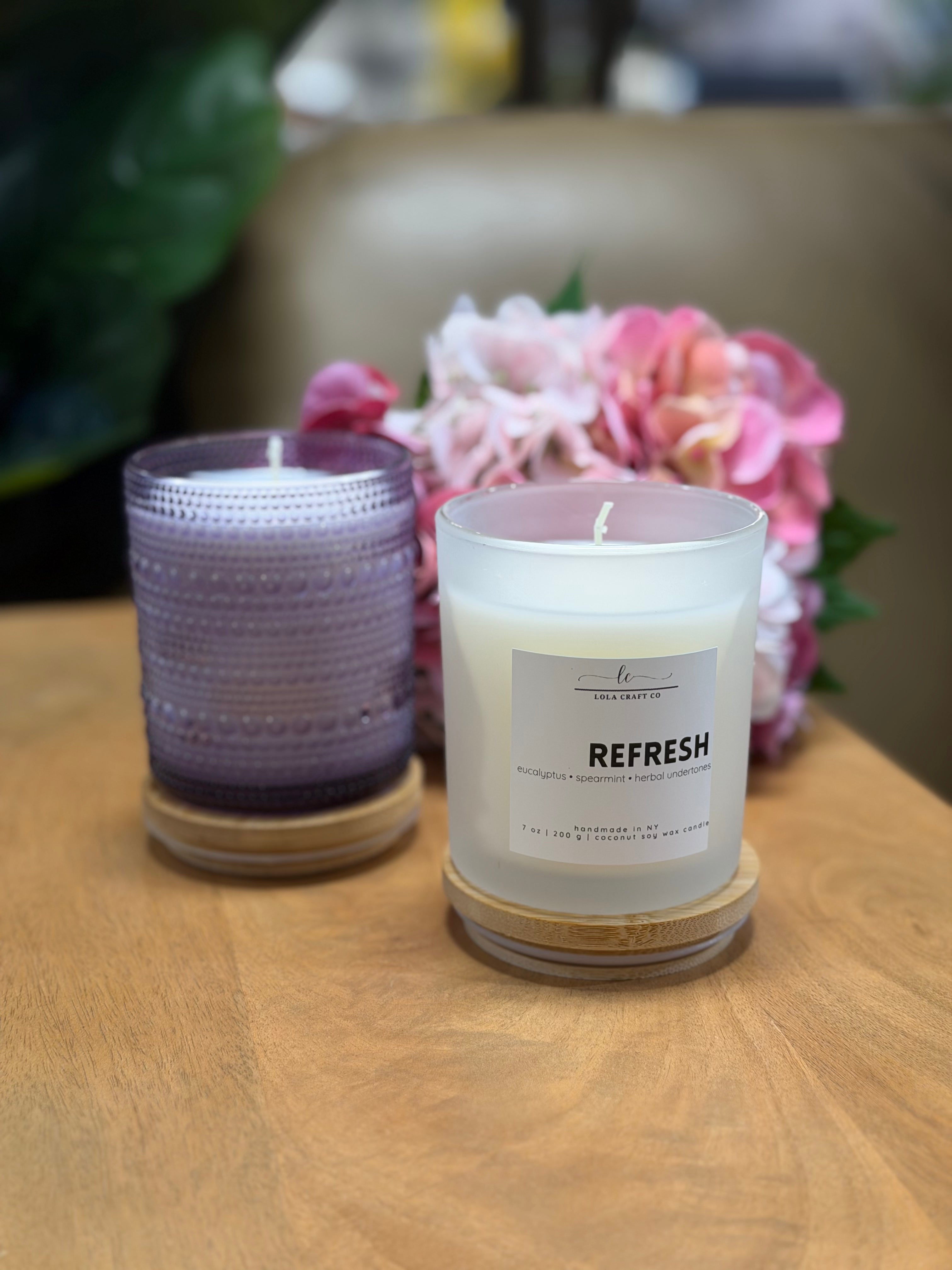 Two candles on a wooden surface with flowers in the background