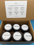 Box of six small containers with labels on a blue background